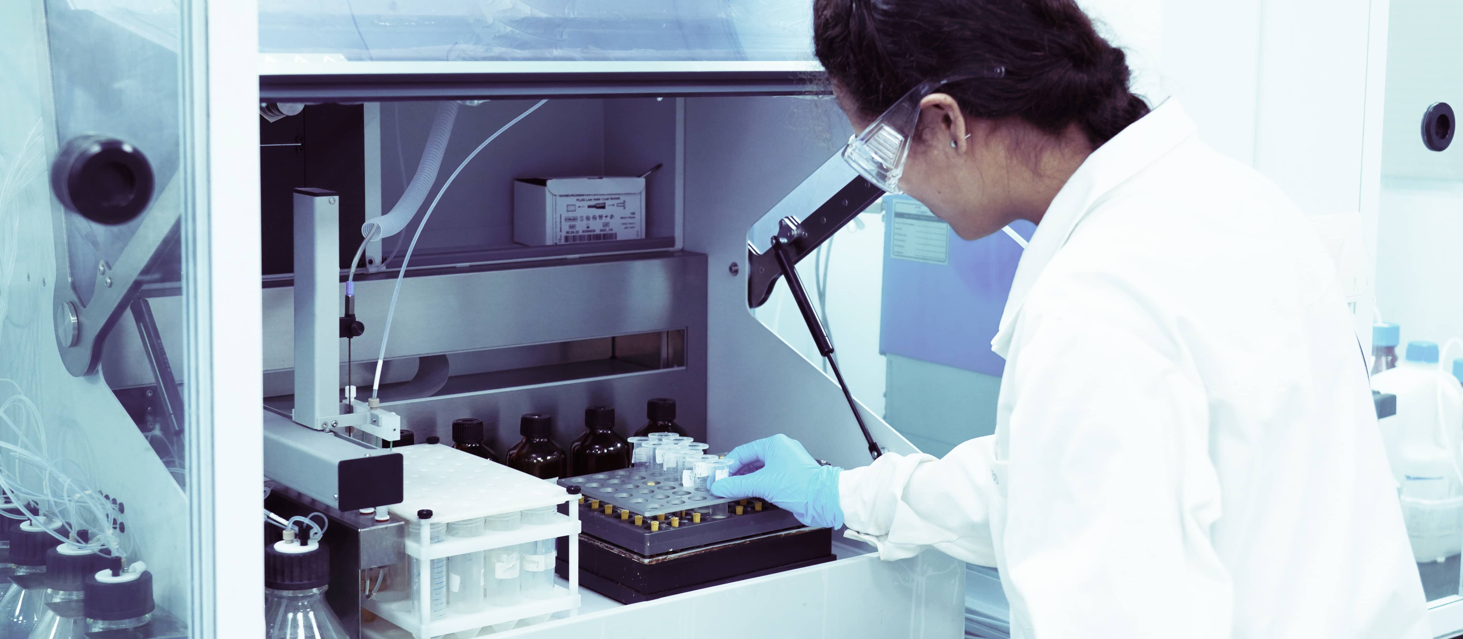 Scientist in safety glasses loading vials into an automated peptide synthesizer