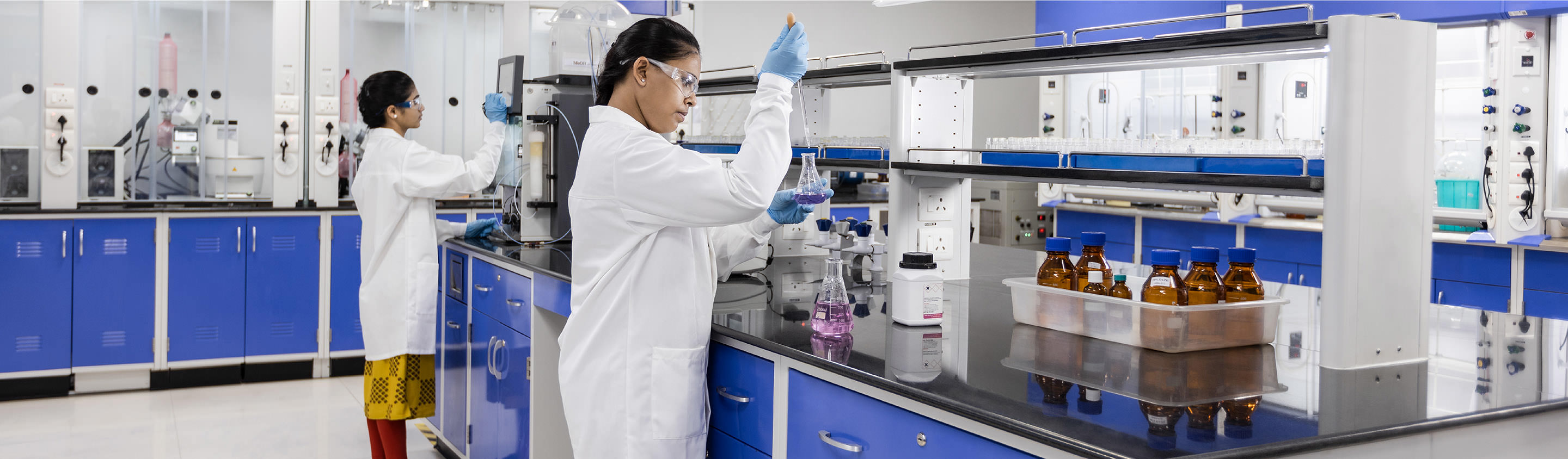 Two Aragen chemists working at fume hoods in a synthetic chemistry laboratory