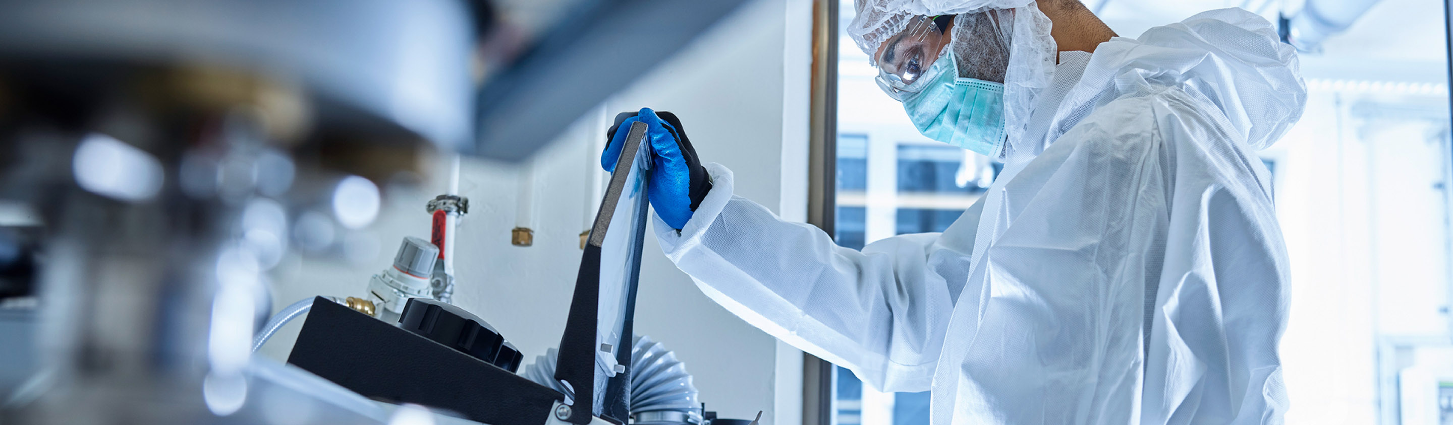 Scientists in cleanroom gowns operating a bioreactor in an Aragen bioproduction facility