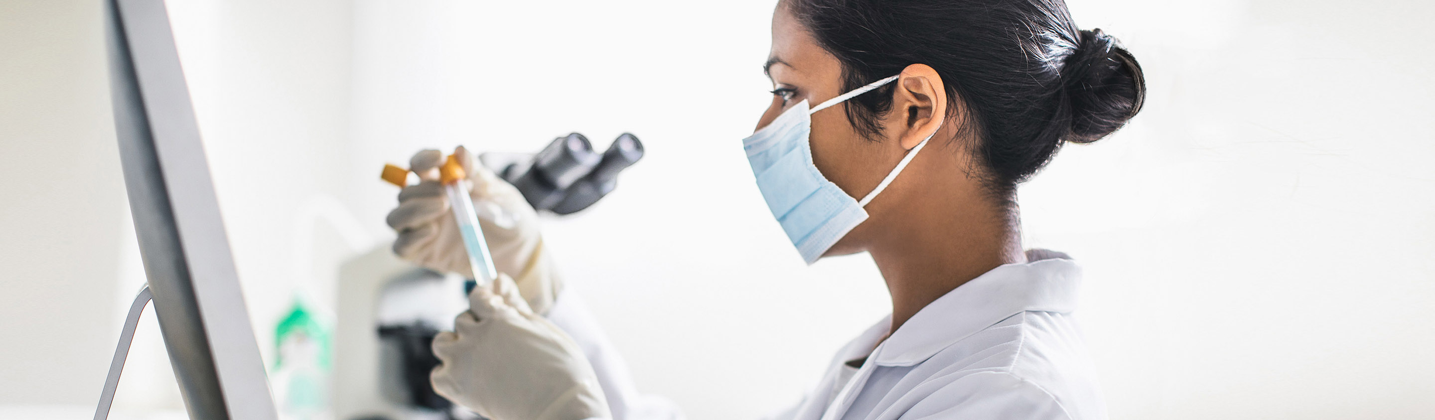 Scientist in mask and lab coat working at a microscope in a molecular biology lab