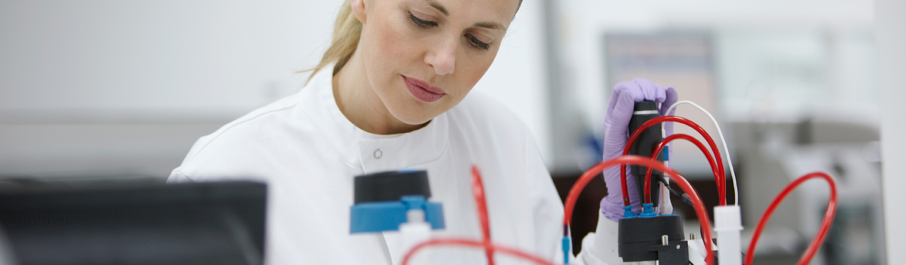 Scientist in lab coat operating laboratory equipment with red tubing