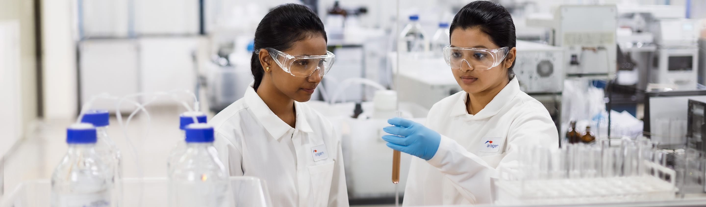 Two Aragen scientists in safety glasses working with glassware at a bench in a safety pharmacology lab