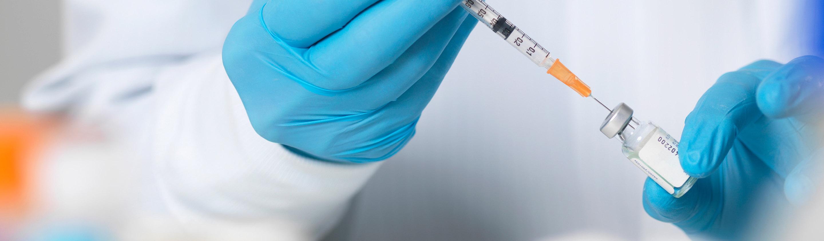 Gloved hands drawing a therapeutic from a vial with a syringe