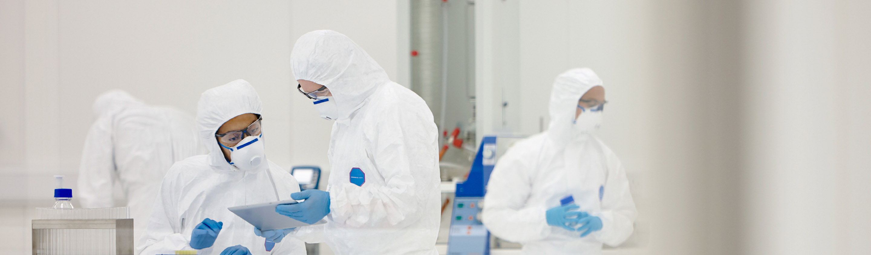 Scientists in cleanroom gowns and gloves working at a bench in an Aragen preclinical research laboratory