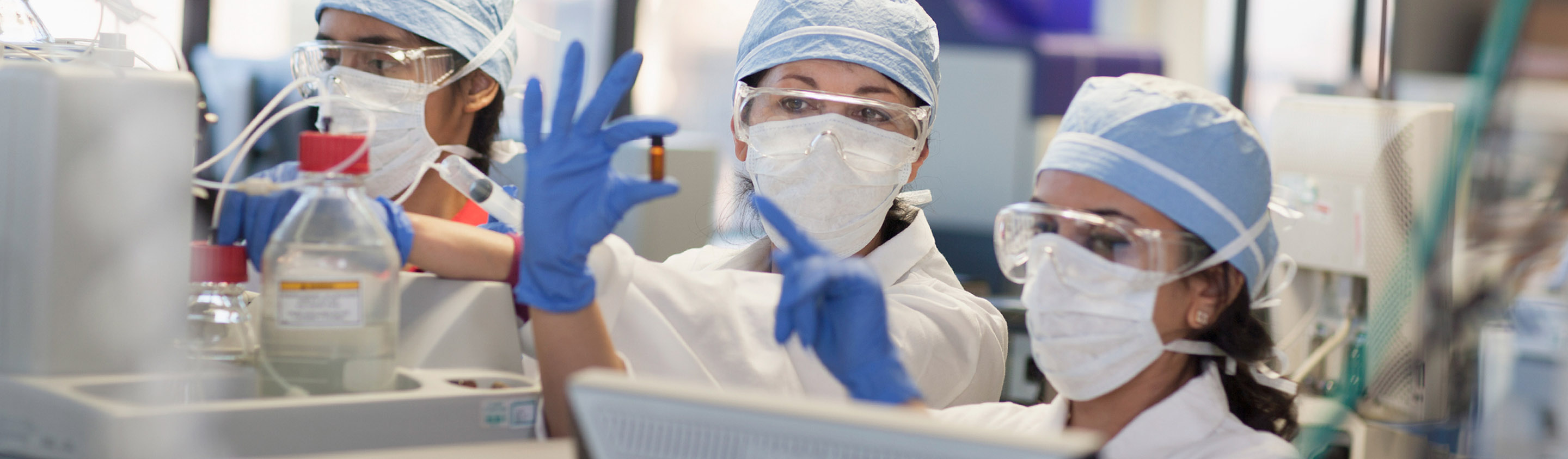 Three Aragen scientists in masks, safety glasses and gloves examining a flask in a toxicology laboratory