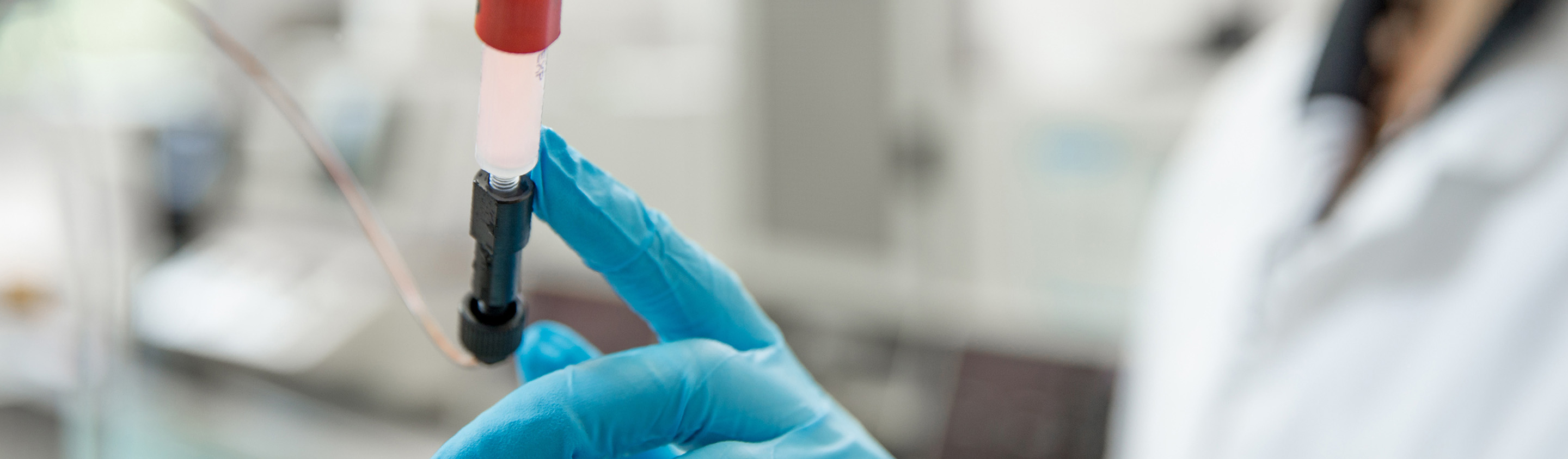 Gloved scientist holding a purification column with red resin for protein expression and purification