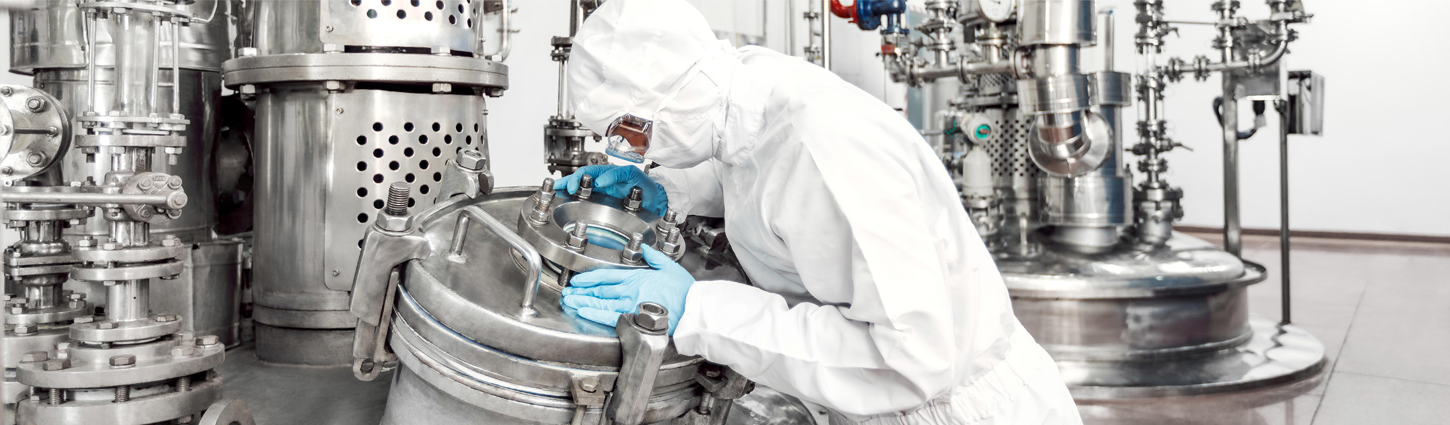 Operator in cleanroom suit working on stainless-steel reactor vessels in an Aragen drug substance manufacturing plant