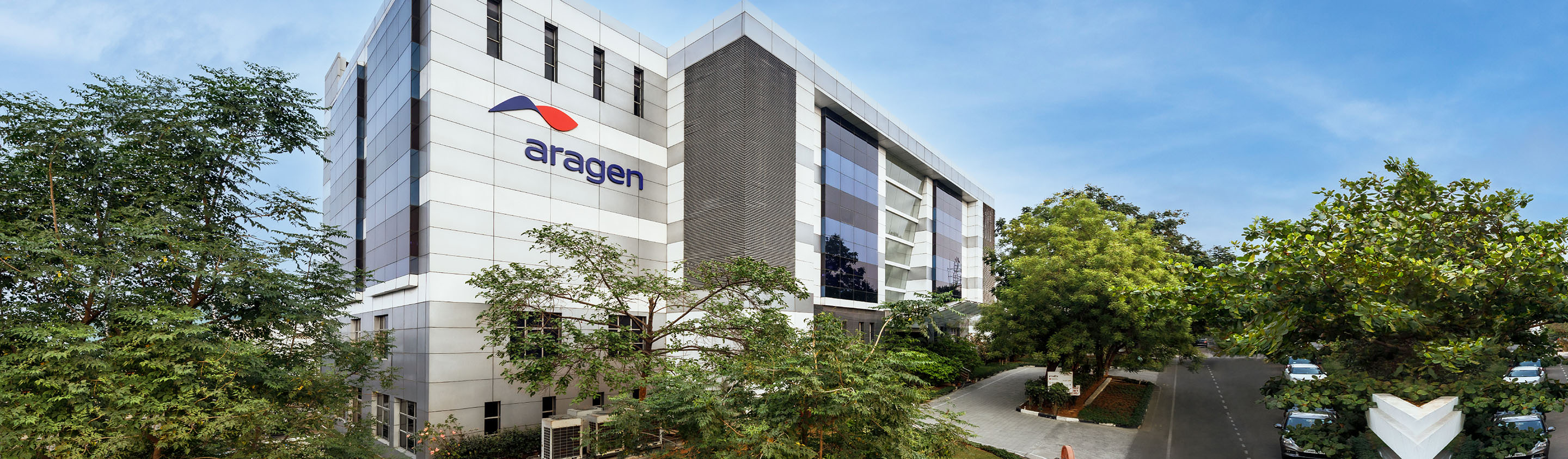 Exterior of the Aragen Life Sciences campus building with the Aragen logo, surrounded by trees