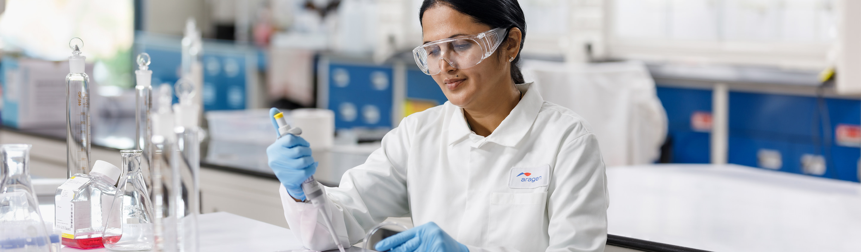 Aragen scientist in safety glasses and gloves examining a sample at a quality control bench