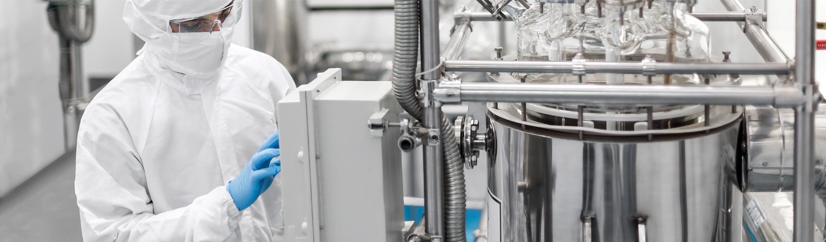 Operator in cleanroom suit adjusting controls on process equipment in a performance chemicals R&D plant