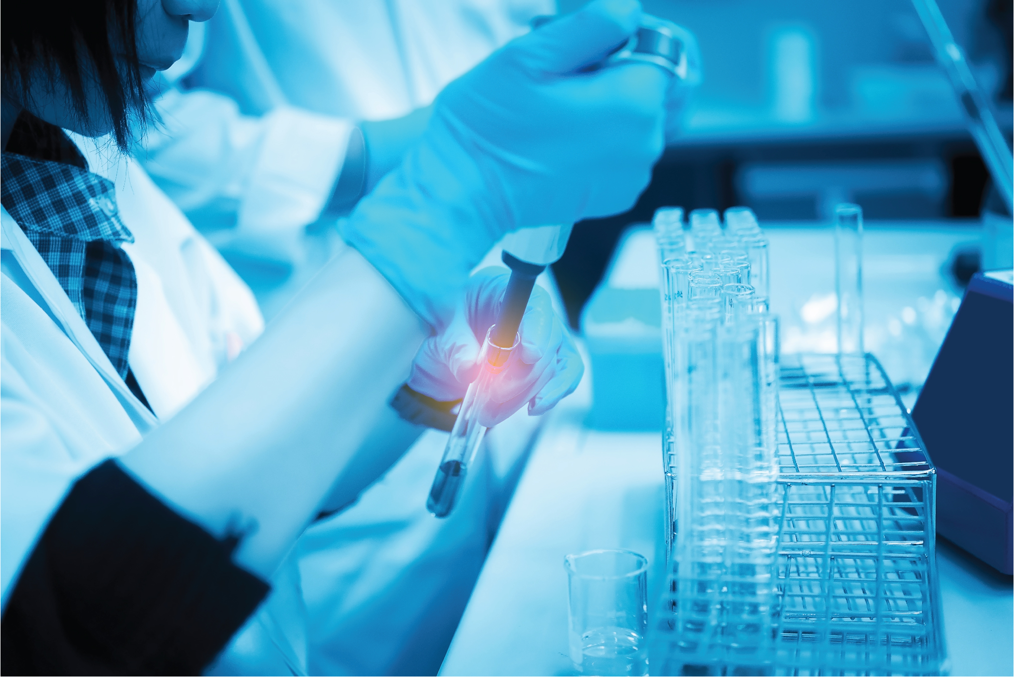 Gloved scientist holding a test tube with red liquid beside a rack of tubes in a blue-lit lab