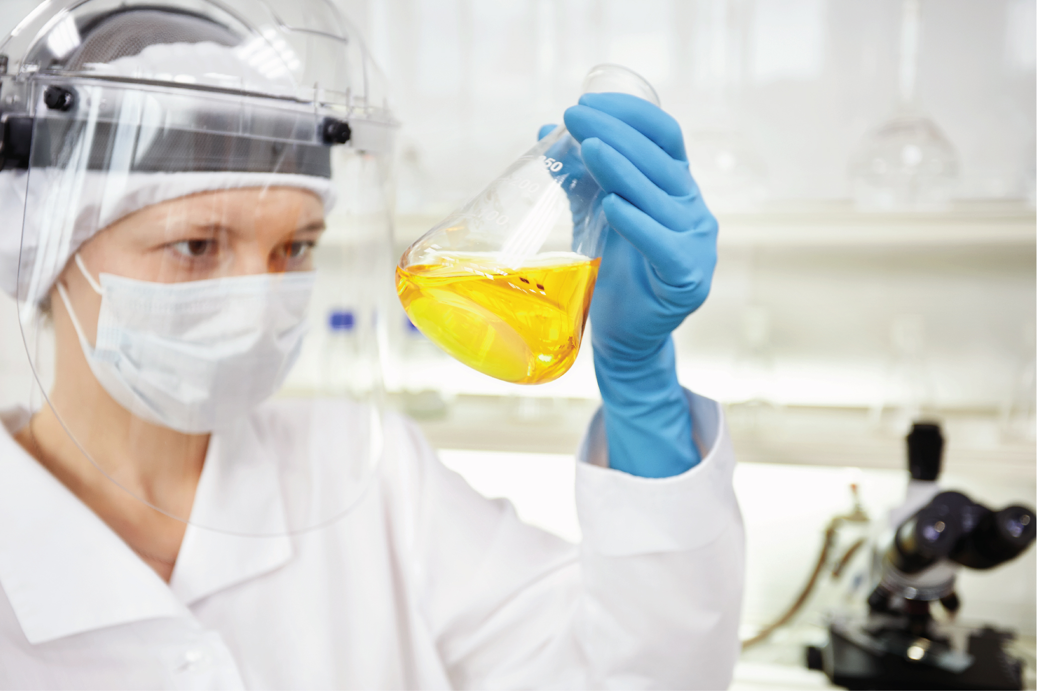 Chemist in face shield and mask holding a flask of yellow solution in a discovery chemistry lab