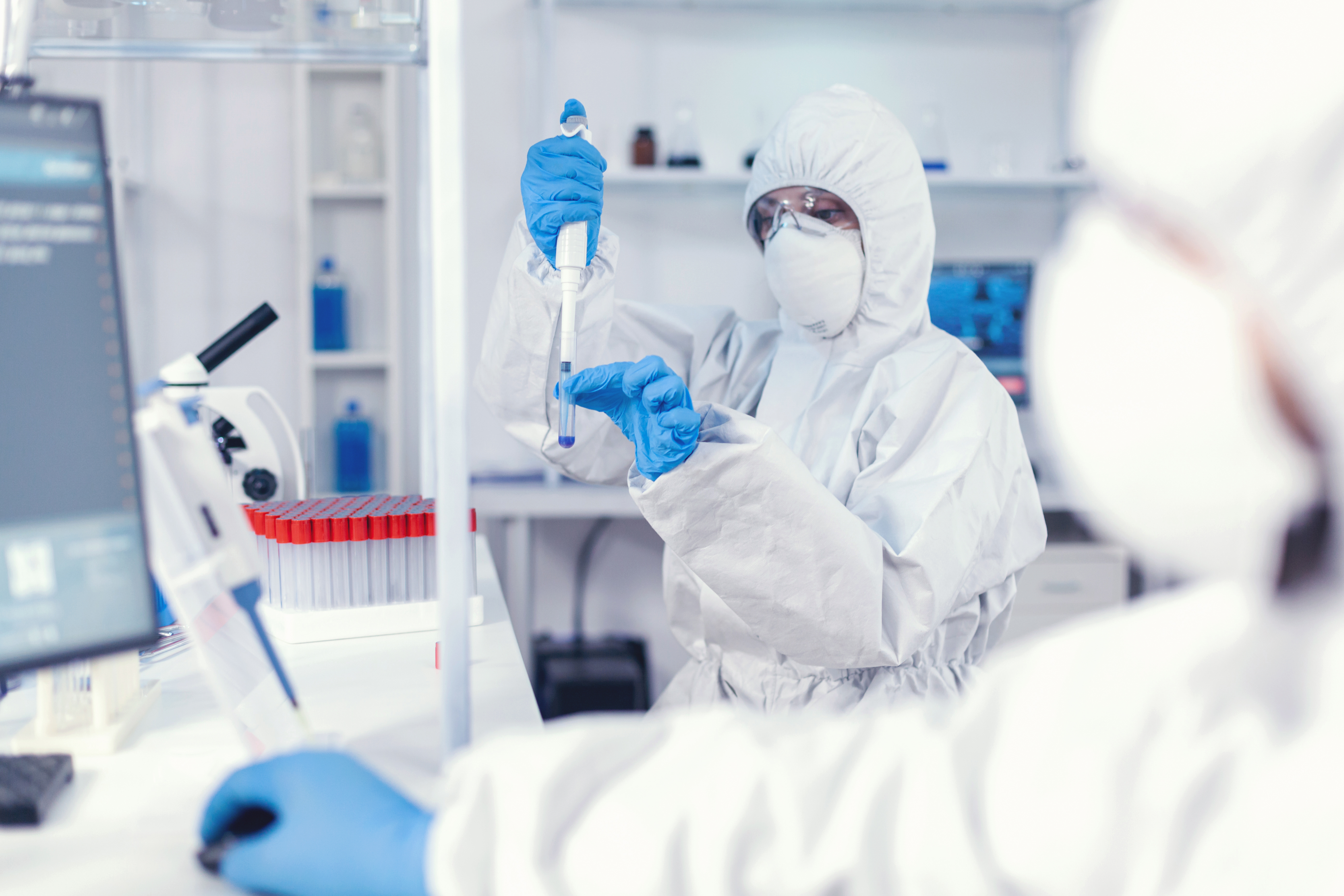 Scientist in full protective suit and goggles pipetting a sample into a test tube in a preclinical laboratory