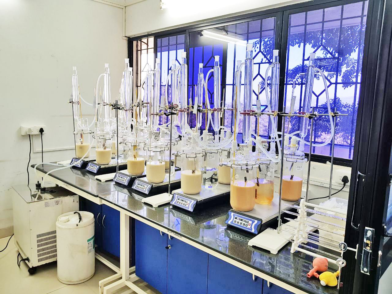 Row of immersion corrosion test setups with glass reaction vessels on heating mantles in an Aragen laboratory
