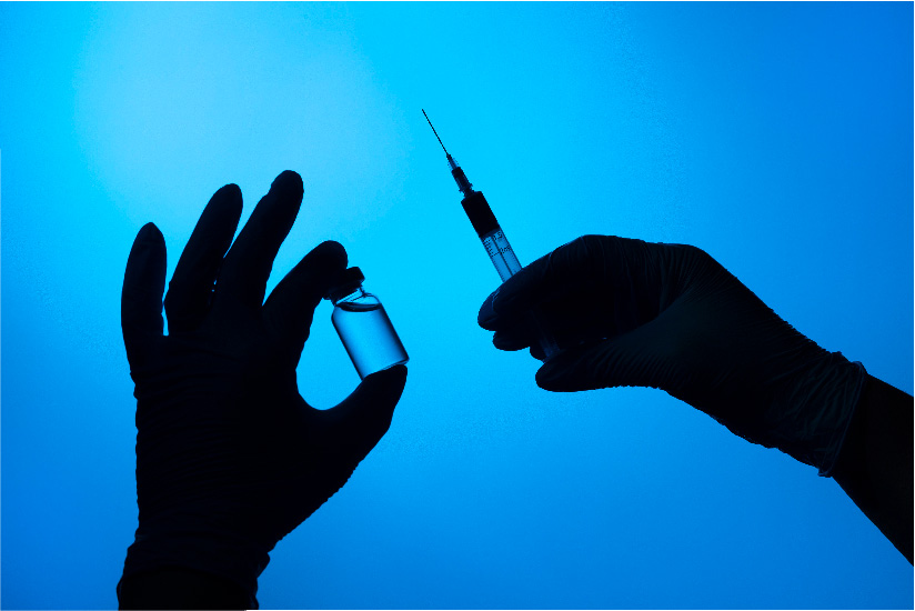 Silhouette of gloved hands holding a vial and syringe against a blue background