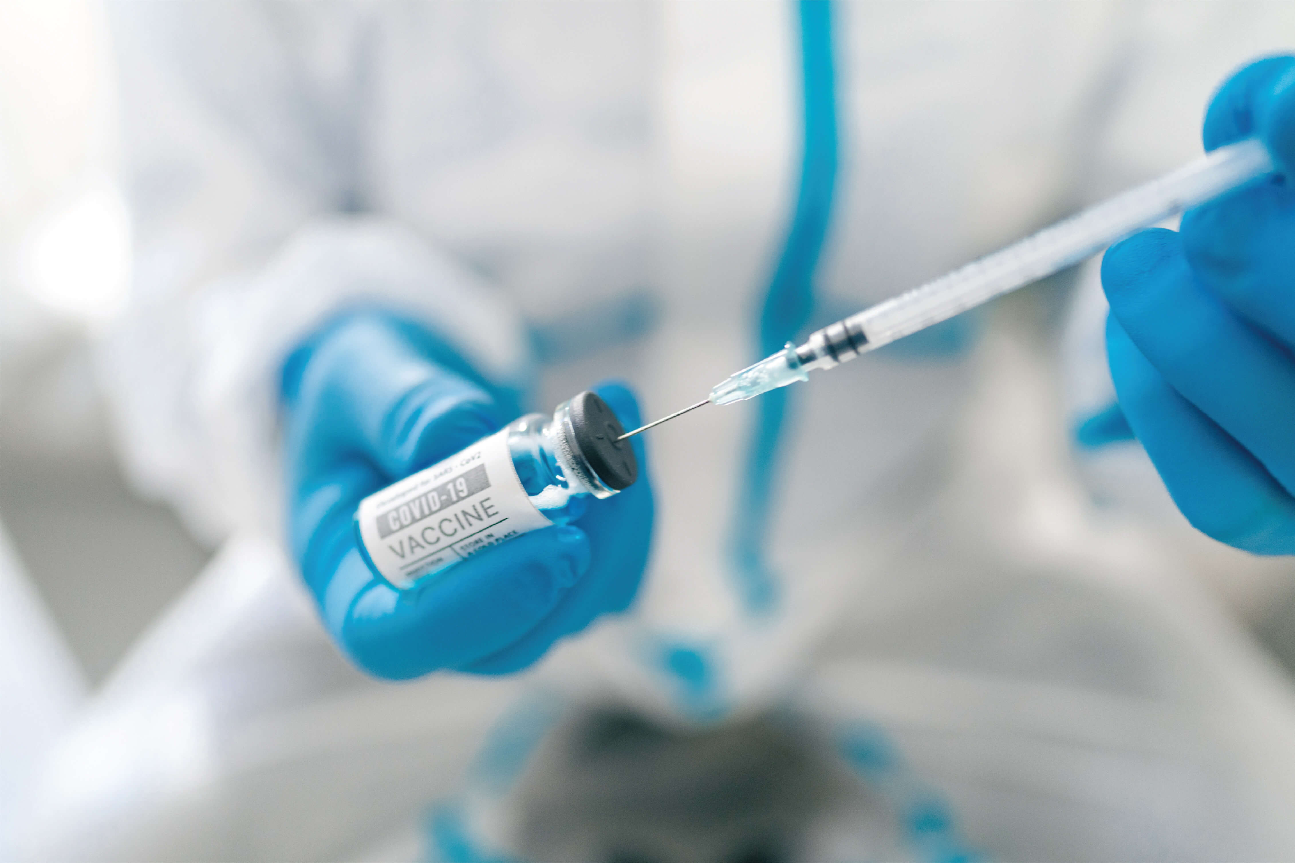 Gloved hands drawing vaccine from a vial with a syringe, representing extractables and leachables testing
