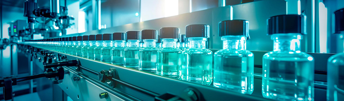 Row of glass vials on a pharmaceutical filling line under blue lighting in a GMP manufacturing facility