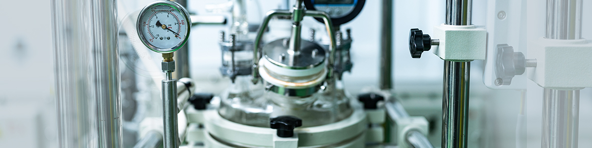 Stainless-steel reactor with pressure gauge and piping in a process scale-up facility