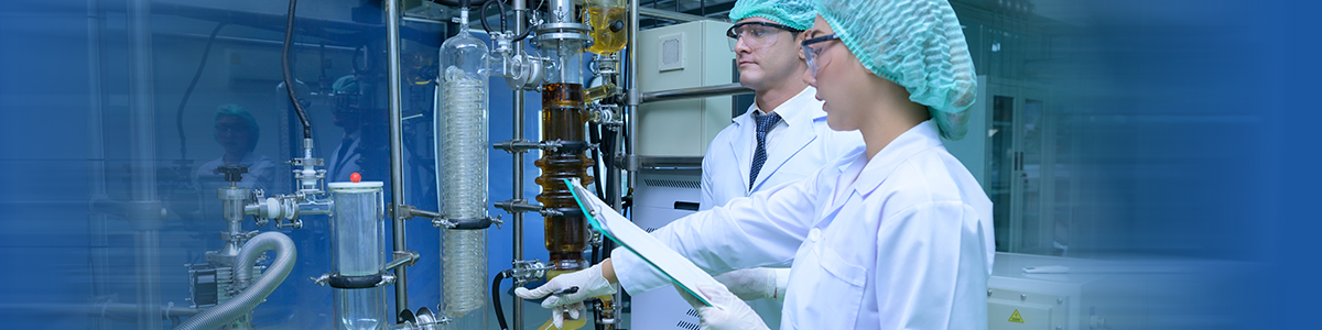 Two Aragen scientists in caps and lab coats reviewing documents beside process equipment