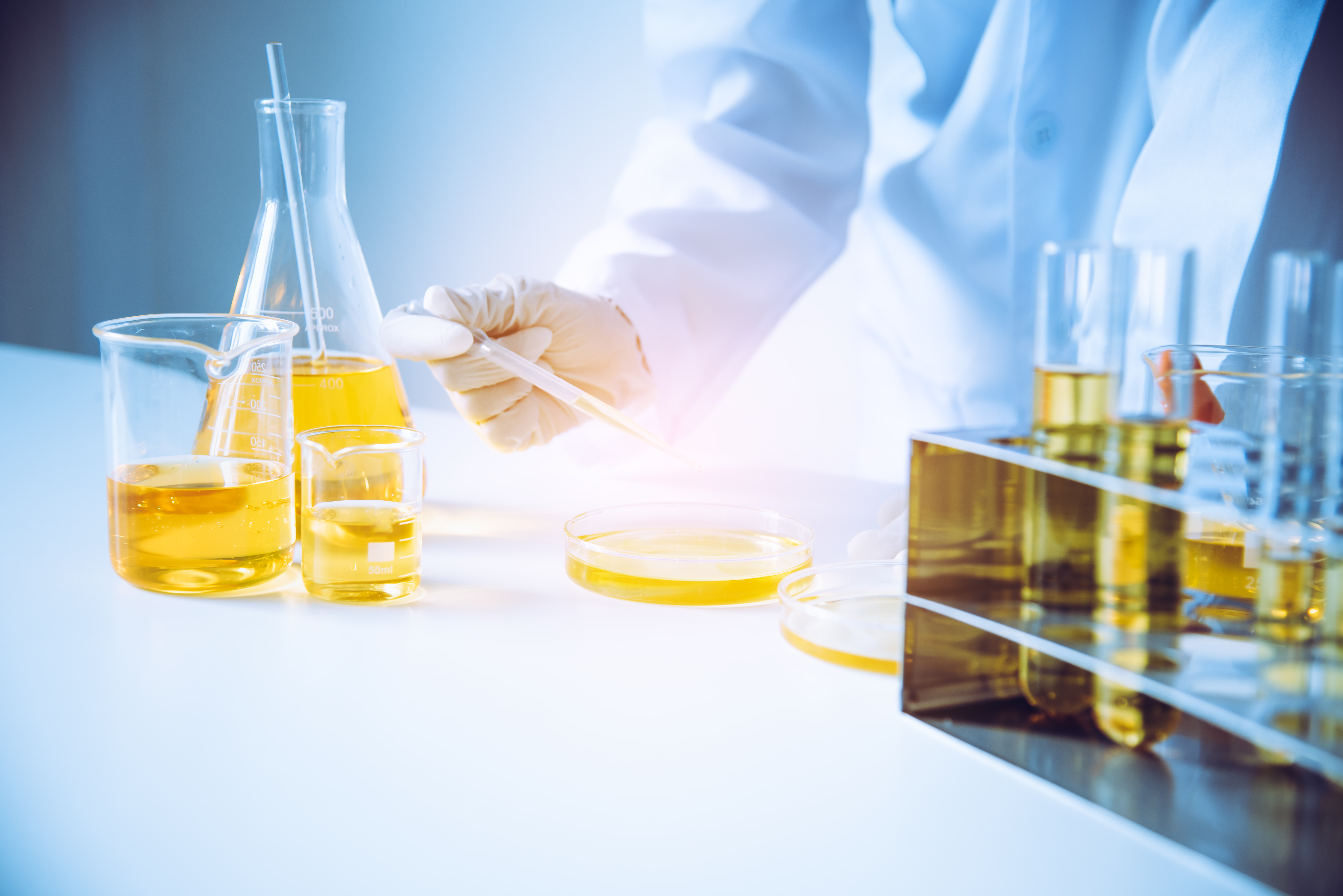Gloved scientist handling yellow solutions in flasks, test tubes and petri dishes, representing covalent therapeutics