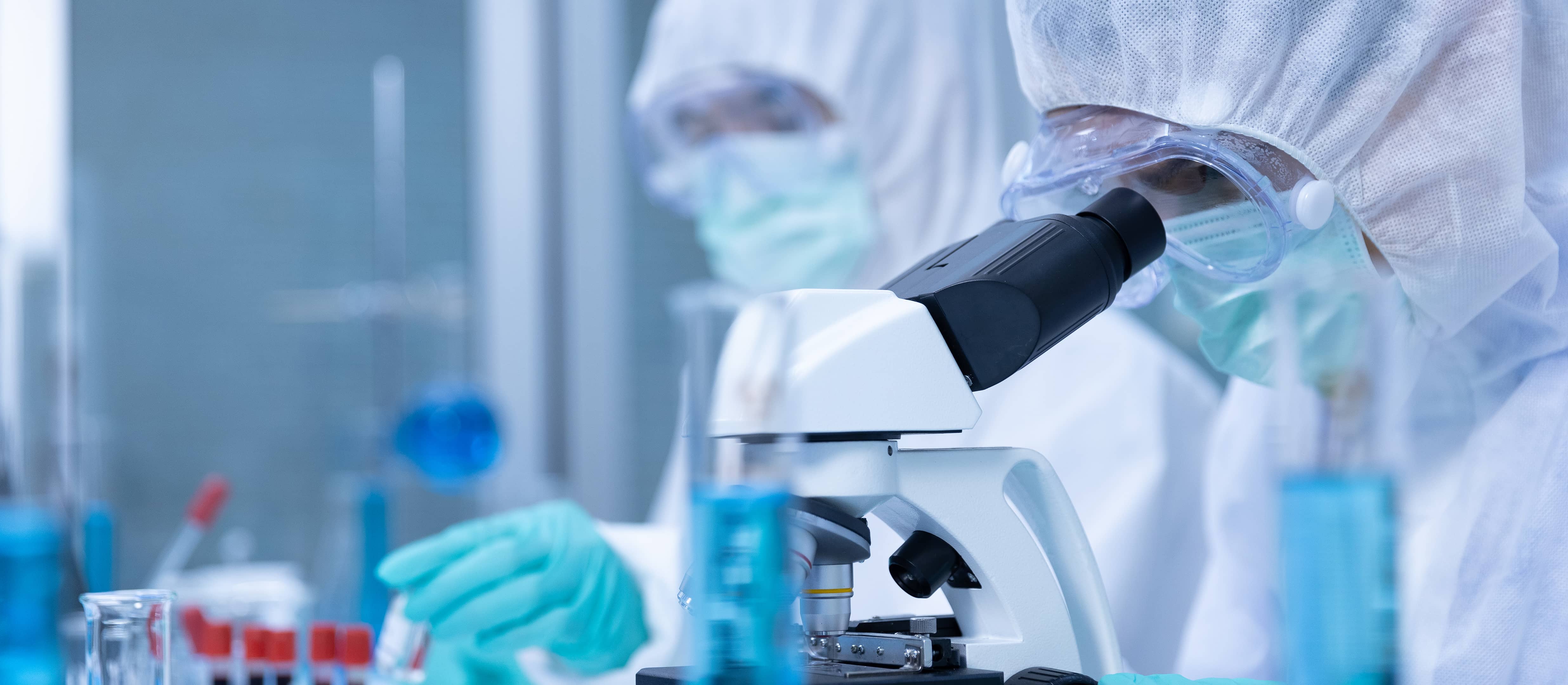 Scientist in protective gear working beside a microscope in a process development laboratory