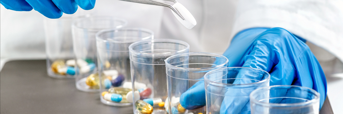 Gloved hand using tweezers to sort colourful capsules into cups, dual-API oral formulation palatability case study banner