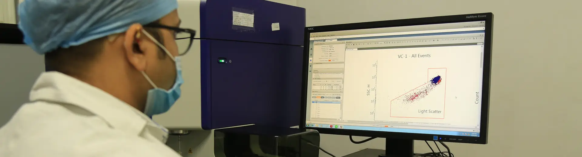 Aragen analyst in lab coat and mask reviewing bioanalysis data on a computer screen beside an instrument